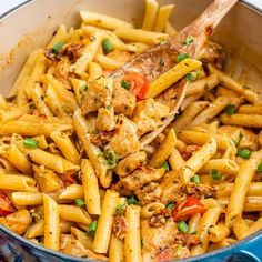 a pan filled with pasta and chicken on top of a blue stovetop next to a wooden spoon