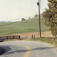 a truck driving down a curvy road next to a lush green field