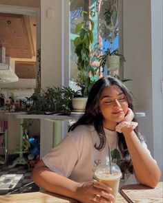 a woman sitting at a table with a drink in her hand and looking off to the side