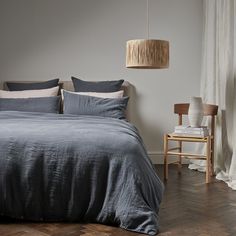 a bed with blue linens and pillows in a bedroom next to a chair, lamp and window