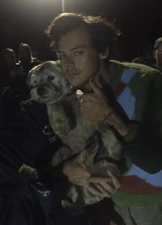 a man holding a small dog in his arms while standing next to other people at night