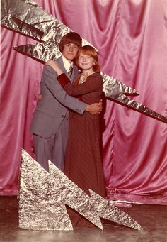 a man and woman hugging each other in front of a pink backdrop with silver foil