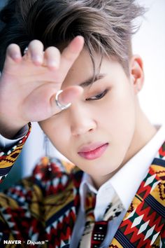 a young man wearing a colorful jacket and tie holding his hand up to his face