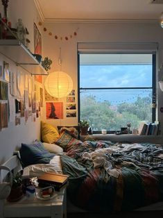 an unmade bed in front of a window with pictures on the wall above it