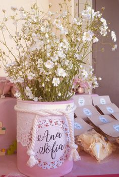 white flowers are in a pink vase on a table with other items and decorations around it