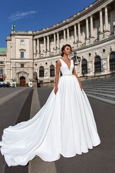 a woman standing in front of a large building wearing a white wedding dress with deep v - neck