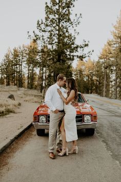 a man and woman standing in front of a red car on the side of the road