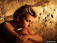 a woman leaning against a stone wall with her arms resting on her chest and looking down