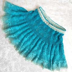 a blue crocheted skirt is laying on a white surface and there are beads hanging from the bottom