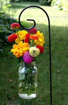 a glass jar filled with flowers hanging from a metal holder on a pole in the grass