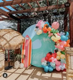 a bunch of balloons are on the ground near a beach hut and umbrellas for people to sit in