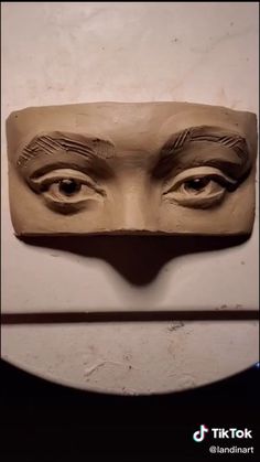 a clay mask with eyes and eyebrows on it's face is shown in front of a white wall