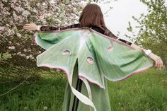 a woman is standing in the grass with a large green butterfly on her shawl