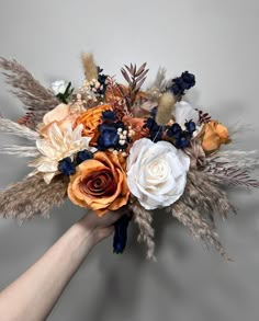 a hand holding a bouquet of flowers on a gray background with white, orange and blue blooms