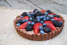 a chocolate tart topped with berries and blueberries on top of a burliege cloth