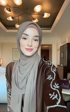 a woman wearing a hijab and smiling for the camera in a hotel room