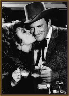 an old photo of a man kissing a woman with a glass in his hand while wearing a hat