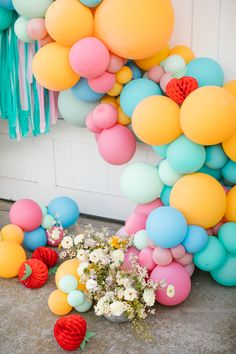 a bunch of balloons and flowers on the ground near a wall with some tassels