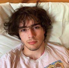 a young man laying in bed with his head on the pillow looking at the camera