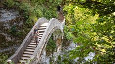 two people are sitting on the stairs leading up to a waterfall in the mountains above them