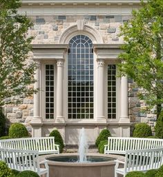 two white park benches sitting next to a fountain in front of a large stone building