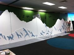 a man is painting a mountain scene on the wall in an office setting with climbing equipment