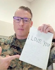 a man in uniform holding up a piece of paper with the words i love you written on it