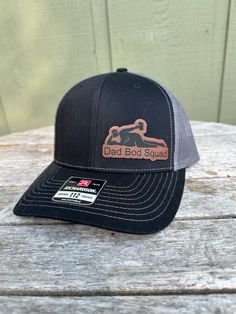 "Dad Bod Squad Hat -  what more is there to say? We also make and sell full custom Patch hats. Wooden patches, leather patches, cork patches, etc. Please see our other listings to place a custom order with your logo or another desired graphic!  Stand out with a high-quality patch adding your business logo or image engraved. We do wood patches, leatherette patches, cork patches, etc.  PRODUCT DETAILS -------------------------- ~ Richardson 112 trucker style snapback hats ~ Add your logo on our high quality custom made hats. ~ Please get in touch with us or view other listings to order bulk orders of 5+ hats!  HOW TO ORDER ----------------------- 1. Select hat color from the drop-down. All colors/styles are shown in a photo in our listing. 2. Please send us a message including your logo file Black Hat With Patches For Outdoor, Black Leather Baseball Cap With Leather Patch, Black Trucker Hat With Leather Patch And Curved Bill, Black Leather Trucker Hat With Leather Patch, Black Snapback Hat With Leather Patch, Black Hat With Leather Patch And Flat Brim, Black Flat Brim Hat With Leather Patch, Black Leather Baseball Cap With Logo Patch, Black Leather Hat With Logo Patch