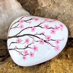 a painted rock sitting on the ground next to a large rock with pink flowers and brown branches