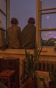 two people are sitting on a window sill looking out at the city below them