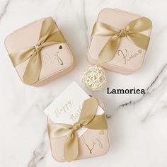 three pink and gold gift boxes with bows on them sitting on a marble countertop