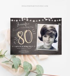 an 80th birthday party card with a photo and string lights on the front, next to eucalyptus leaves