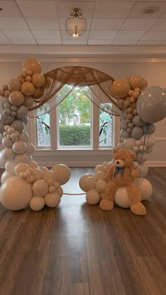 a teddy bear sitting on top of a wooden floor next to balloons in front of a window