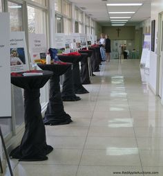 there are many tables lined up in the hallway with signs on them and people looking out the windows