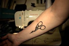 a person with a tattoo on their arm holding a pair of scissors in front of a sewing machine