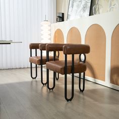 three brown chairs sitting in front of a white wall