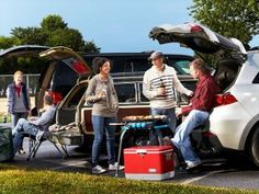 three people are sitting in the back of a car with their trunk open and one person standing next to them