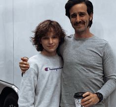 a man standing next to a little boy in front of a food truck holding a coffee cup