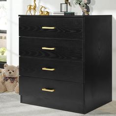 a black chest of drawers with gold handles and knobs on each drawer, in a white room