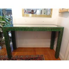 a green console table sitting on top of a hard wood floor next to a mirror