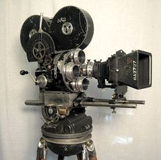 an old movie projector sitting on top of a tripod in front of a white wall