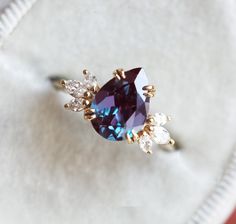 a ring with an amethyst colored stone surrounded by white and gold diamonds on a cloth