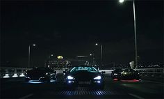 two cars driving on a highway at night time with city lights in the background,