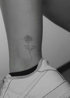 a black and white photo of a woman's foot with a single rose tattoo