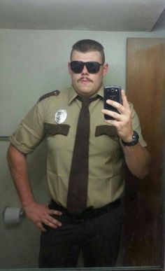 a police officer taking a selfie in the mirror with his cell phone and sunglasses on