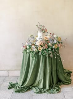 a wedding cake on top of a green table cloth with flowers and greenery around it