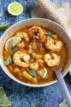 a bowl of soup with shrimp, lime and cilantro on the side next to a spoon