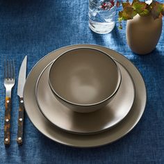 there is a silver plate with two forks and a knife on the blue table cloth