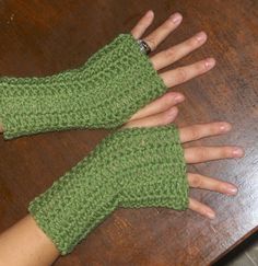 two hands wearing green knitted mittens on top of a wooden table