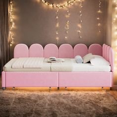 a pink bed with lots of lights on the wall above it and a rug in front of it